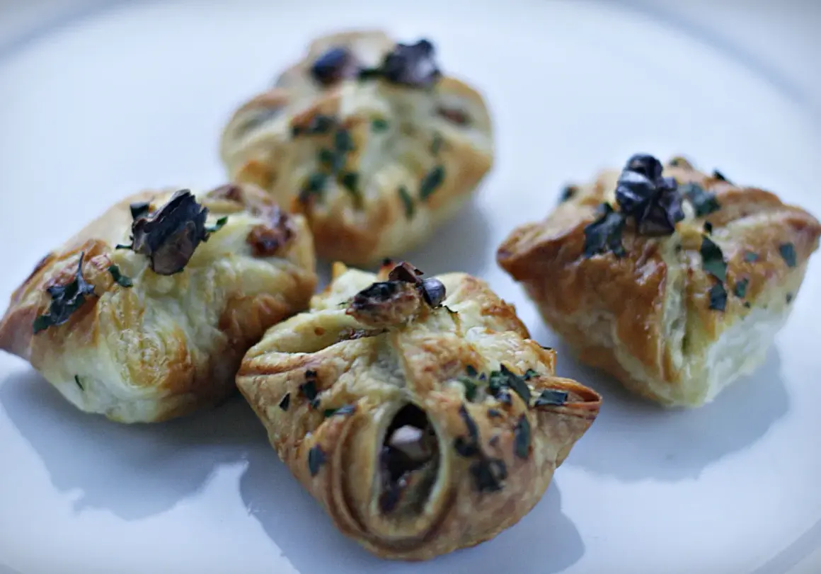 Cztery apetyczne paczuszki z ciasta francuskiego z gruszką i serem pleśniowym, posypane ziołami.
