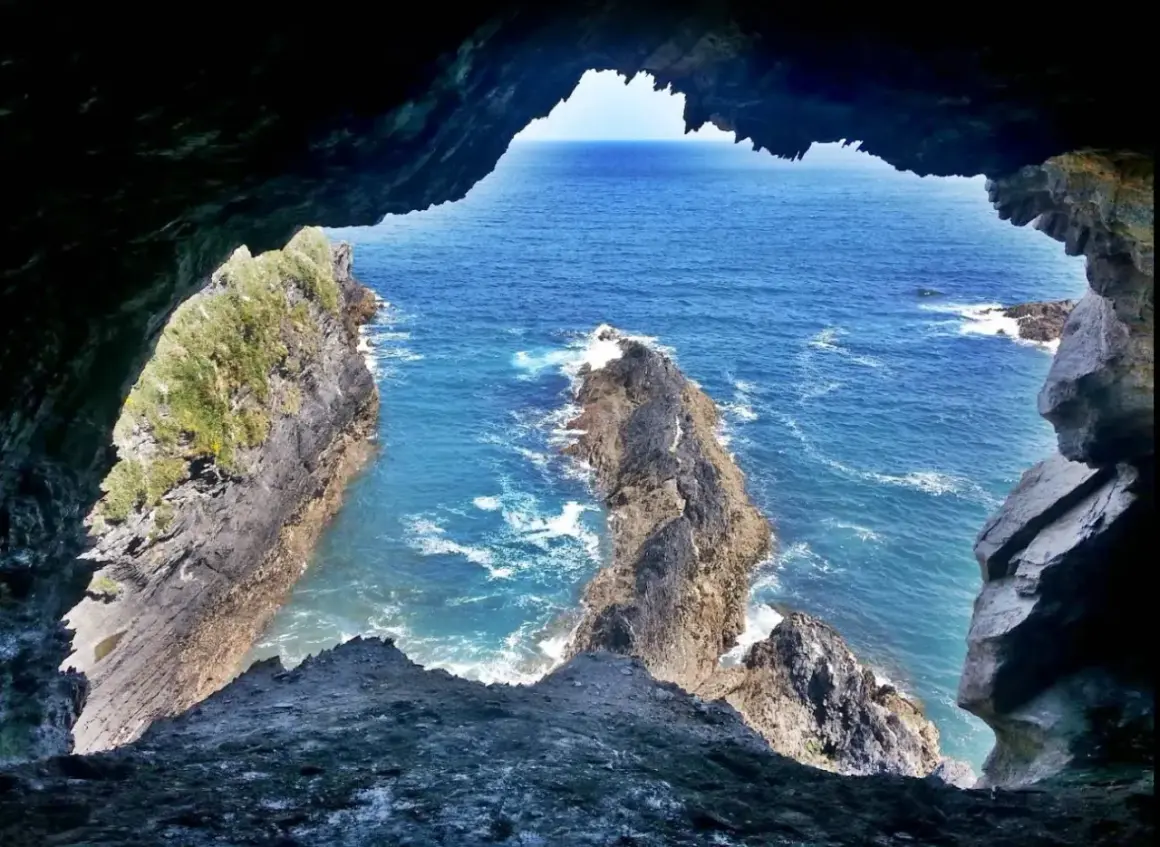 Vista desde la Cova da Doncela hacia el mar azul y acantilados rocosos.
