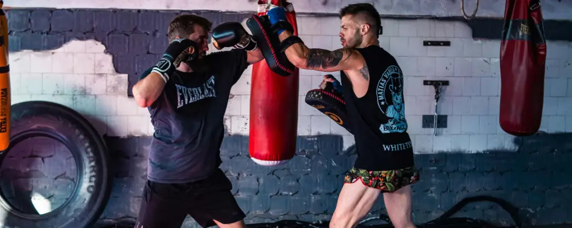 Two boxers train in a gym. One throws a punch while the other uses pads to parry boxing.