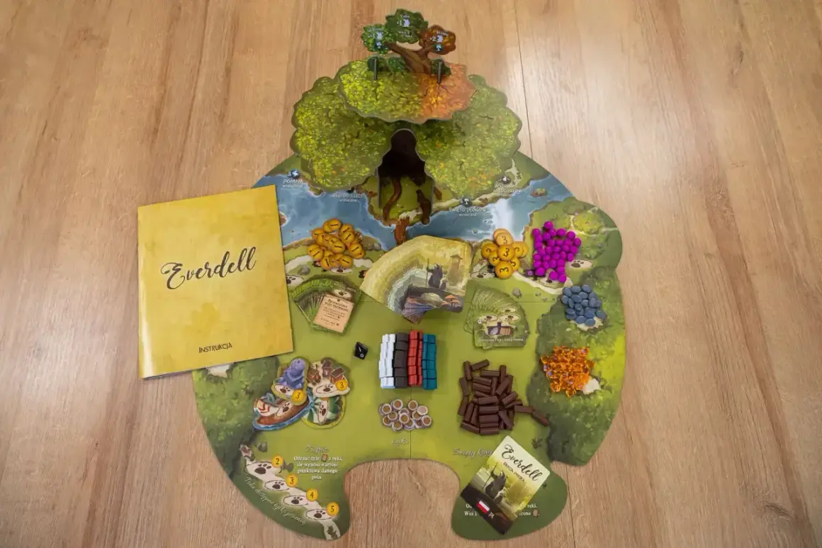 Na drewnianym tle leży plansza gry Everdell z instrukcją. Widać kolorowe zasoby, karty i pionki.