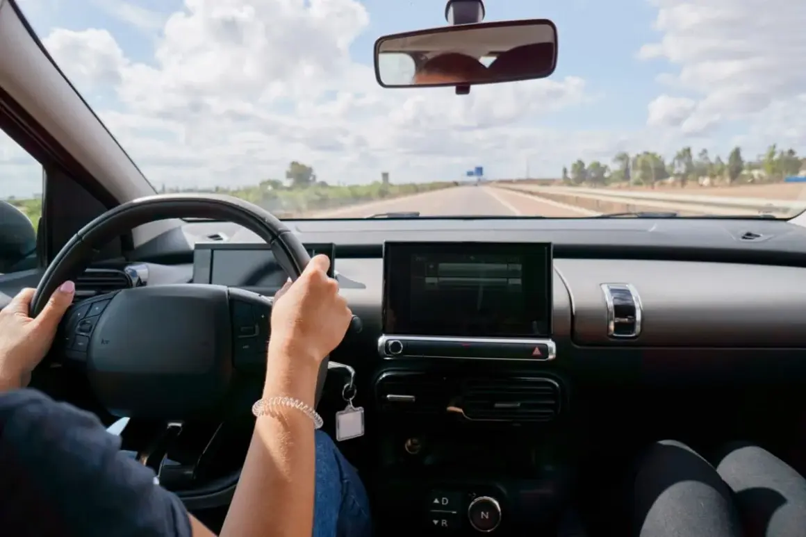 Vue du **rétro intérieur position nuit** d'une voiture. Mains sur le volant, route dégagée sous un ciel nuageux.