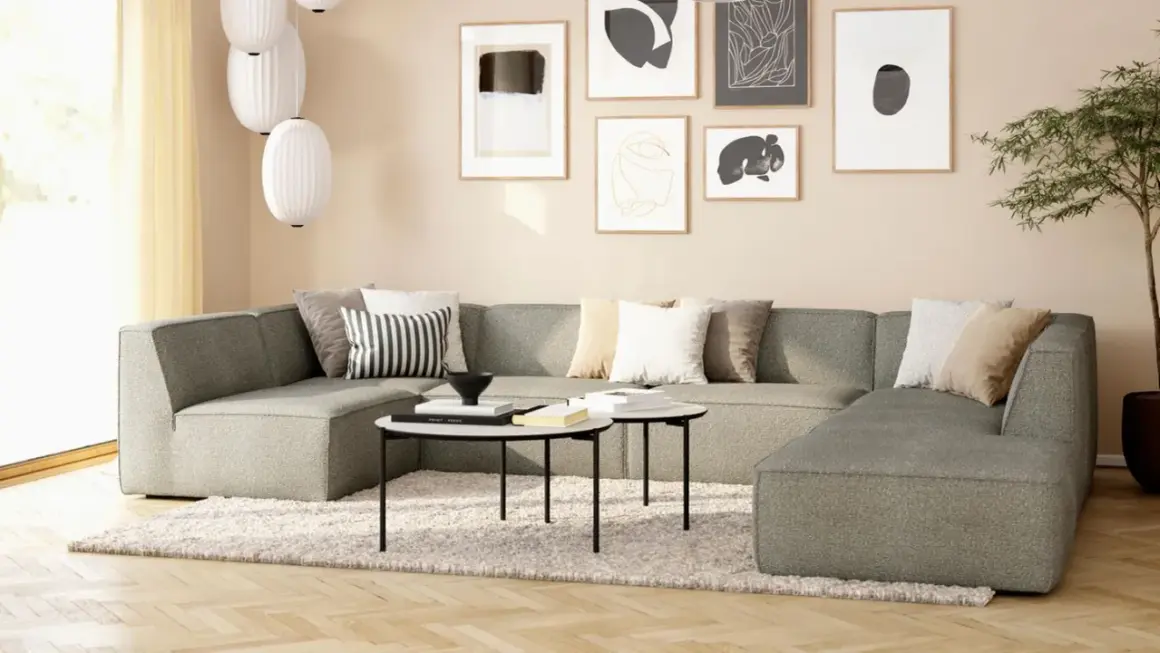 Gemütliches Wohnzimmer mit beiger Wand, einem großen grauen Sofa, Kissen und Kunstwerken.