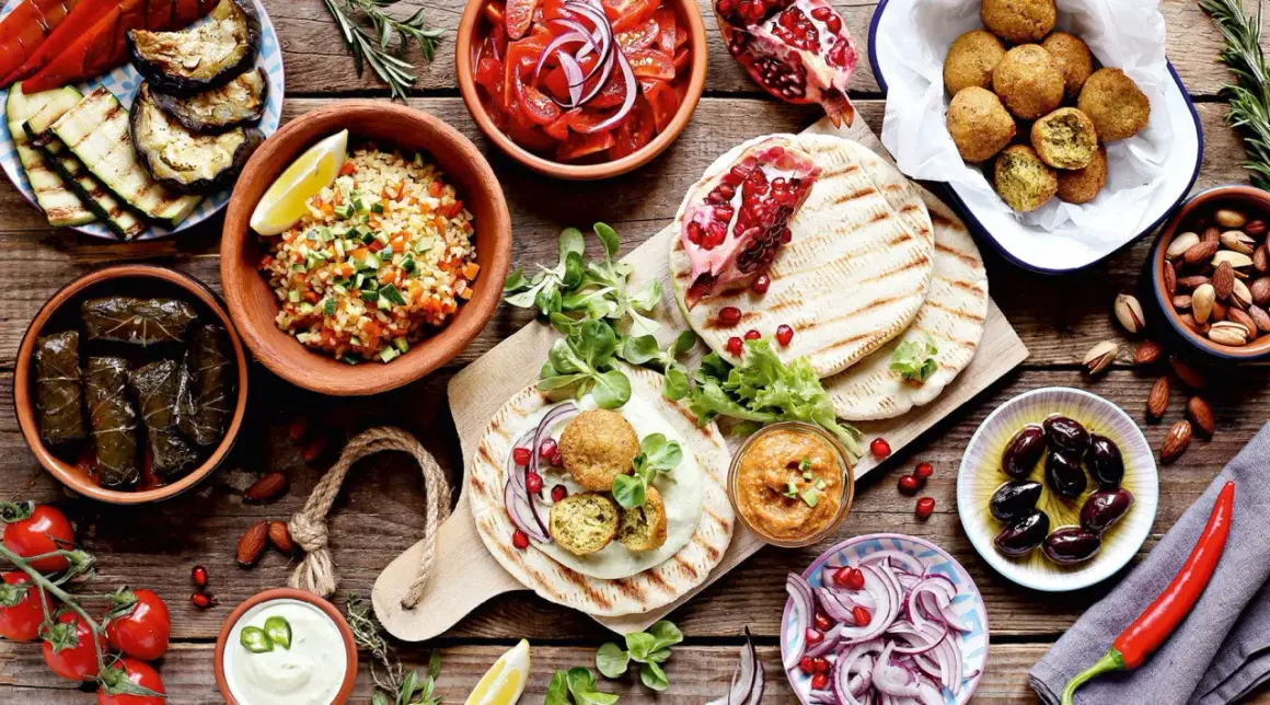 Vielfalt an arabischem Essen: Falafel, gefüllte Weinblätter, Bulgursalat, gegrilltes Gemüse, Hummus, Oliven und Granatapfel.