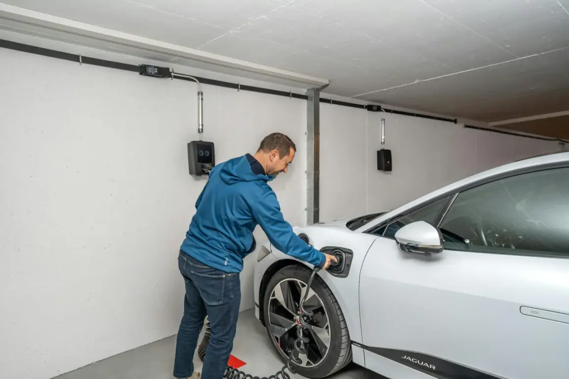 Mann lädt ein Elektroauto in der Garage. Die Installation ist für den Brandschutz ausgelegt.