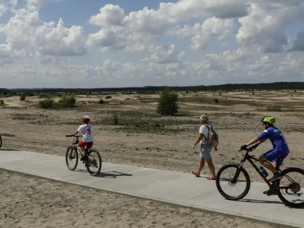 Ludzie na rowerach i pieszo na ścieżce rowerowej w krajobrazie pustynnym.