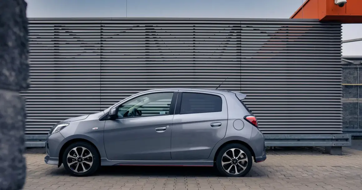 Szary Mitsubishi Space Star stoi na tle nowoczesnej, szarej ściany z poziomymi żaluzjami.