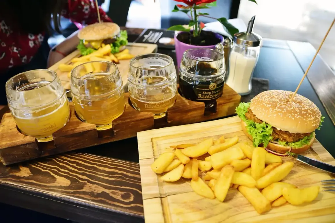 Degustacja piw z Browaru Rzeszowskiego: trzy kufle z jasnym i ciemnym piwem, obok burgery i frytki.