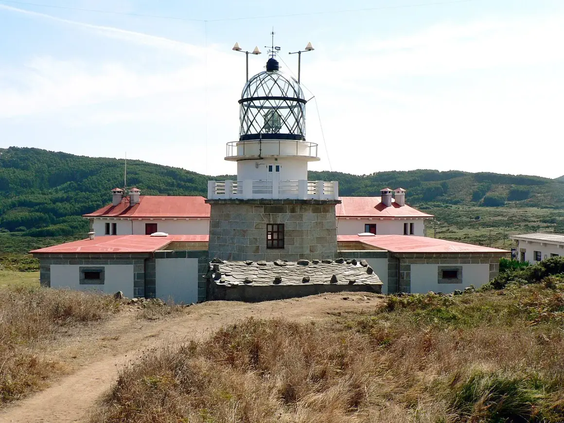 El faro de estaca de bares se alza imponente sobre la costa, con sus edificios blancos y tejados rojos rodeados de vegetación.