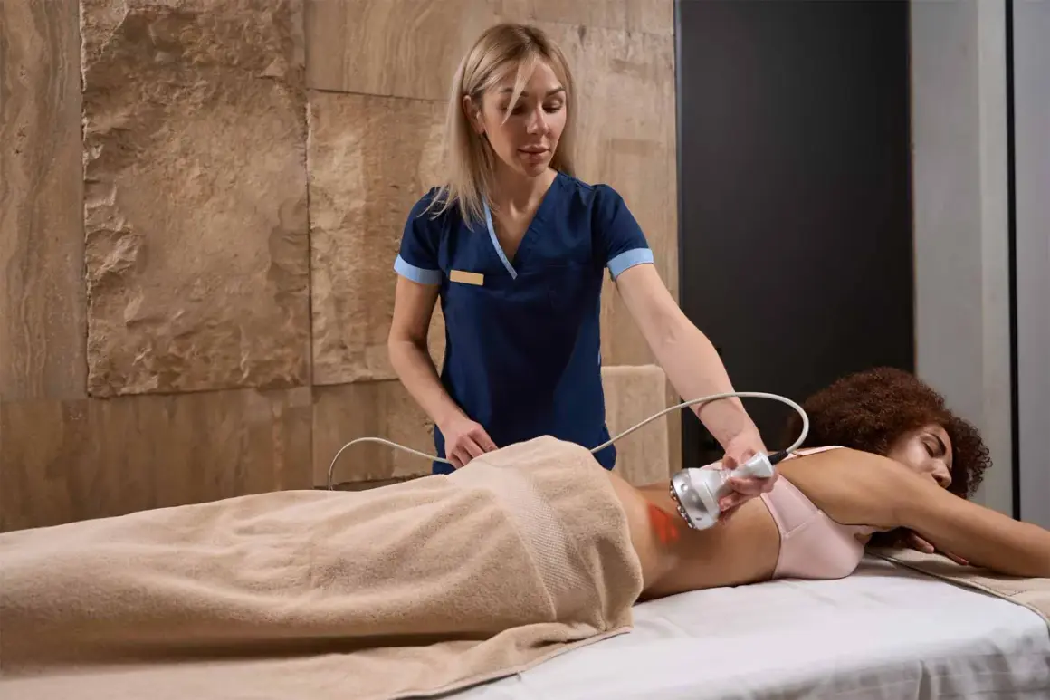 Terapista esegue crioterapia fisioterapia su paziente sdraiata, usando un manipolo con luce rossa sulla schiena.