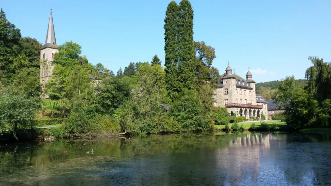 Schloss und Kirche in Wiehl Gummersbach, umgeben von üppigem Grün und einem ruhigen See.