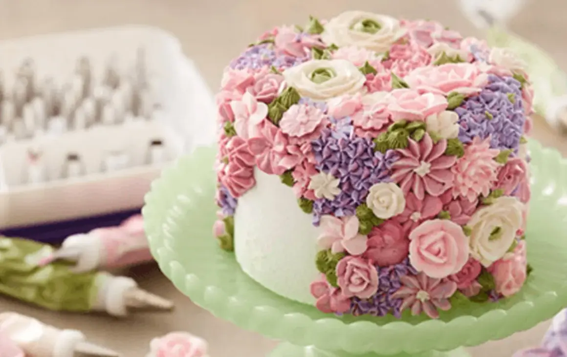En tårta täckt av vackra blommor skapade genom att spritsa tårta med frosting i rosa, lila och gröna nyanser.