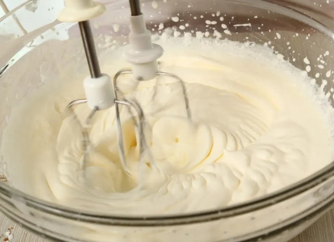 Ubity krem śmietankowy do tortu bez mascarpone, przygotowywany mikserem w szklanej misie.