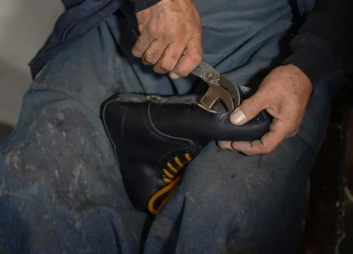 Mains d'un cordonnier travaillant sur une chaussure simili cuir qui s'effrite, utilisant une pince pour la réparer.