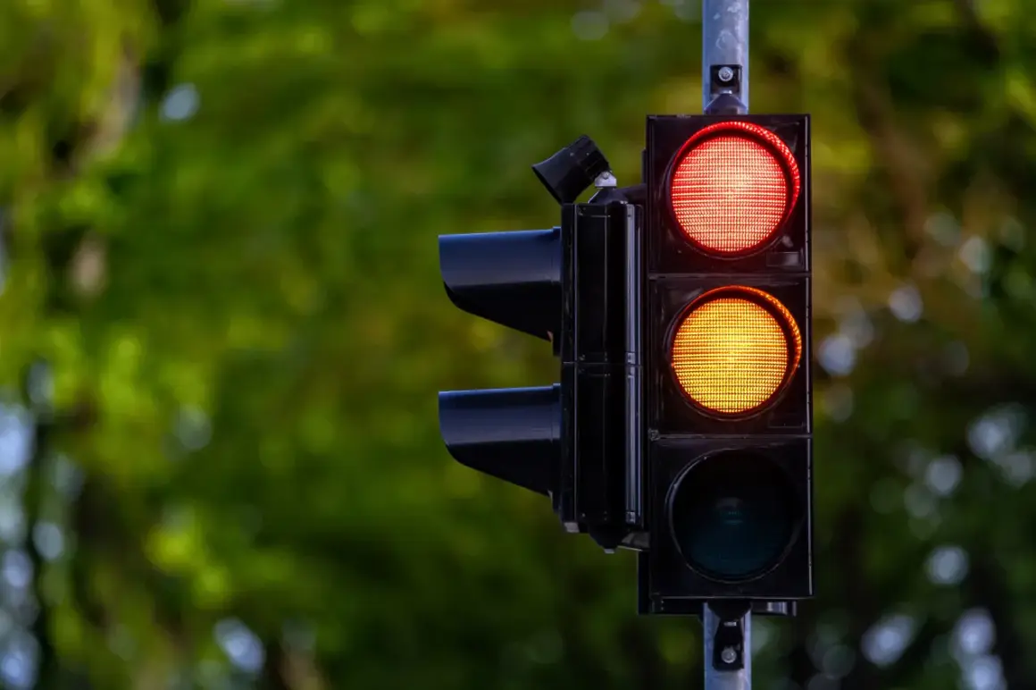 Sygnalizacja świetlna z czerwonym i żółtym światłem. Kierowca zastanawia się, czy zdąży na przejazd na żółtym świetle, czy lepiej zahamować.
