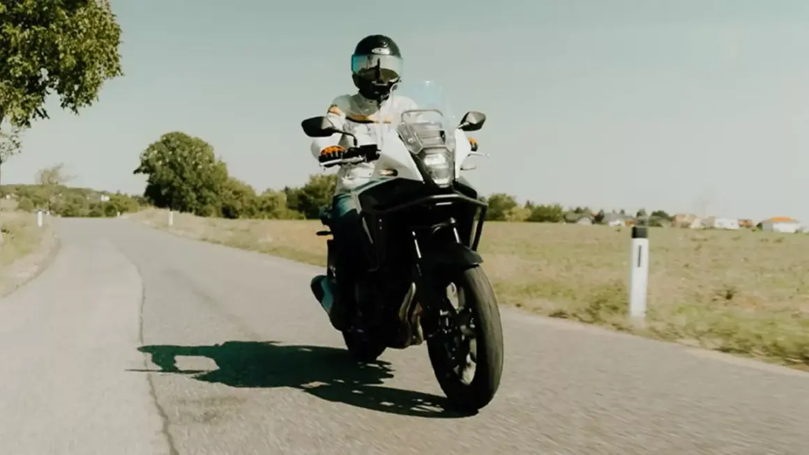 Motocyklista w kasku jedzie motocyklem turystycznym po wiejskiej drodze. Idealny na kategorię A2.