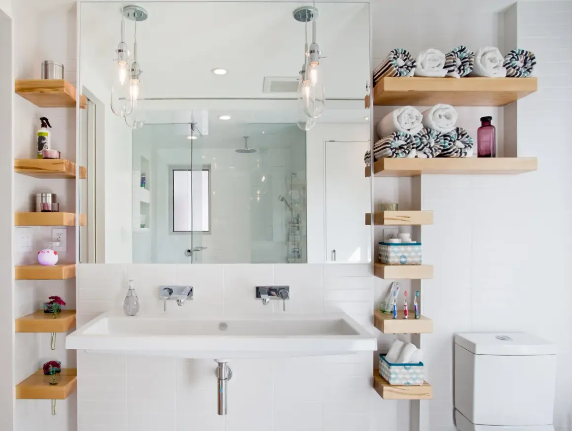 Salle de bain petite surface : lavabo double, étagères en bois flotté, miroir, douche vitrée et toilettes. Idée déco fonctionnelle.