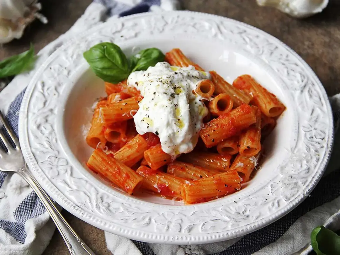 En krämig burrata pasta med rigatoni i tomatsås, toppad med färsk basilika och svartpeppar.