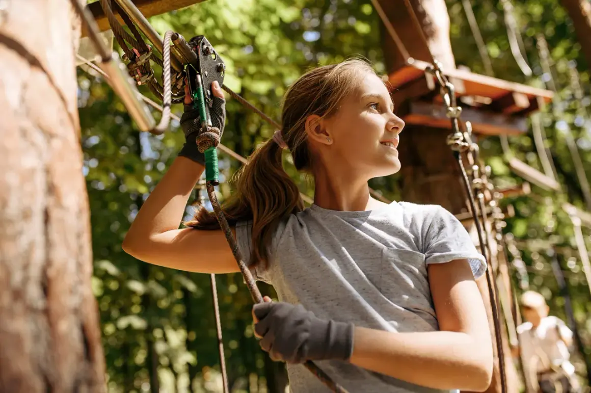 Ein Mädchen mit Zopf genießt den Ausblick im Kletterpark Wuppertal, während sie sich an einem Seil festhält.