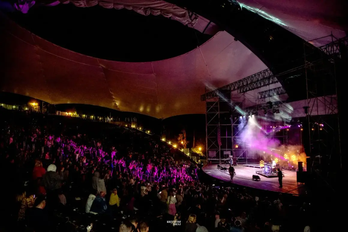 Koncert na amfiteatrze w Mrągowie, oświetlona scena i publiczność.