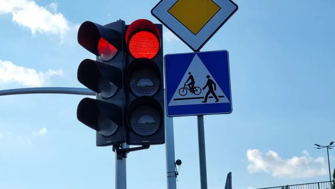 Czerwone światło na sygnalizatorze drogowym, obok znak d6 informujący o przejściu dla pieszych i rowerzystów.