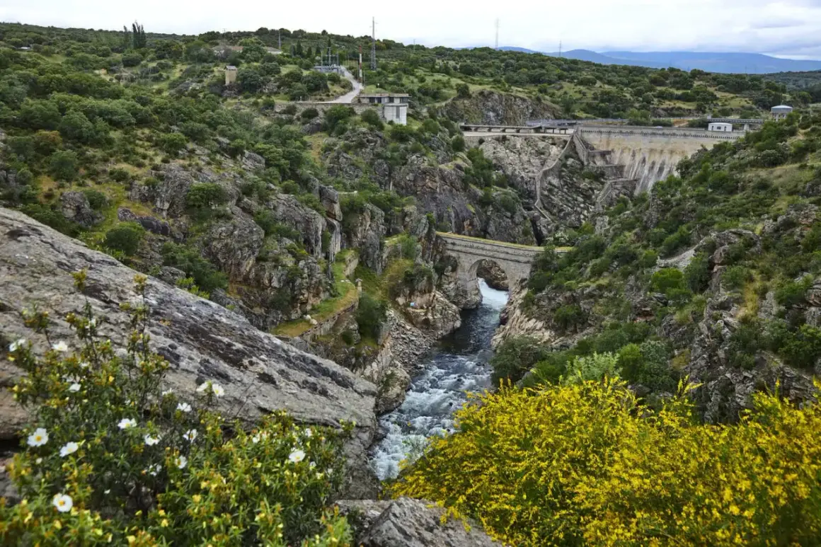 Paisaje natural con un río caudaloso, un puente de piedra y una presa. Un lugar ideal que ver en Robledillo de la Jara para disfrutar de la naturaleza.