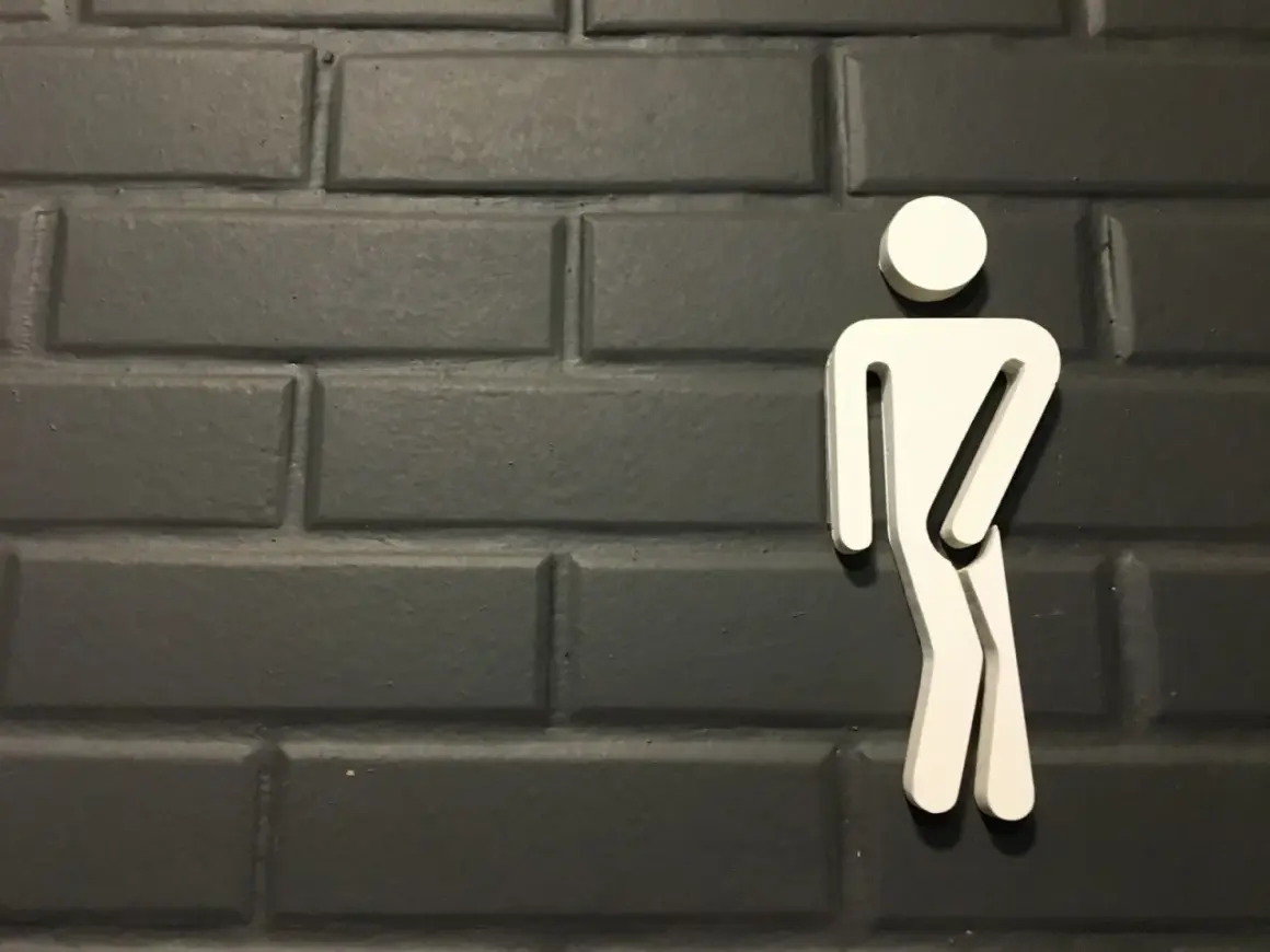 Biały symbol mężczyzny na ciemnej, ceglanej ścianie. Może symbolizować problemy z oddawaniem moczu, takie jak niskie ciśnienie moczu u mężczyzn.