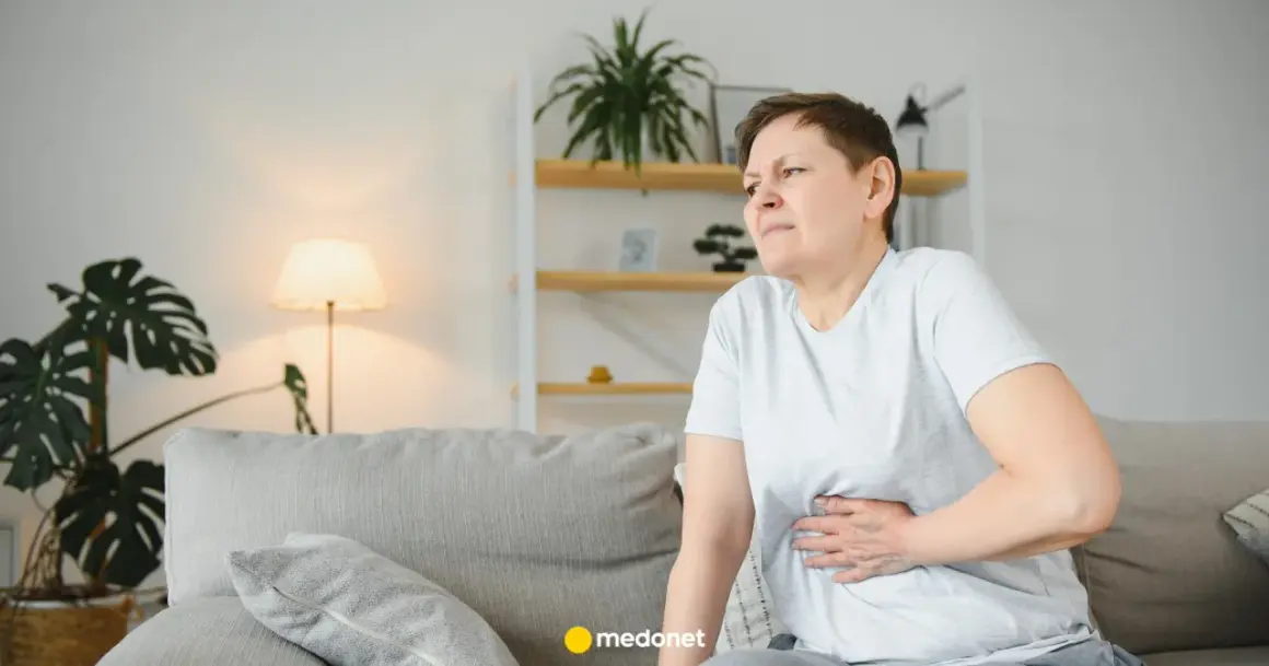 Kobieta z bólem brzucha, być może potrzebuje metoclopramidum polpharma. Siedzi na kanapie w salonie.