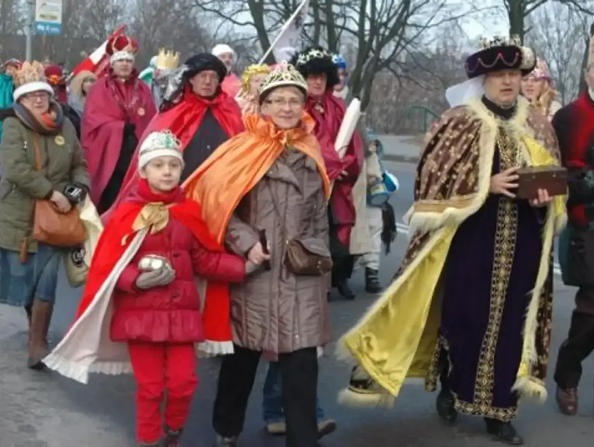 Kolorowe stroje Trzech Króli na ulicznym orszaku. Dziecko w czerwonym płaszczu i koronie, obok dorosłe osoby w bogatych szatach.