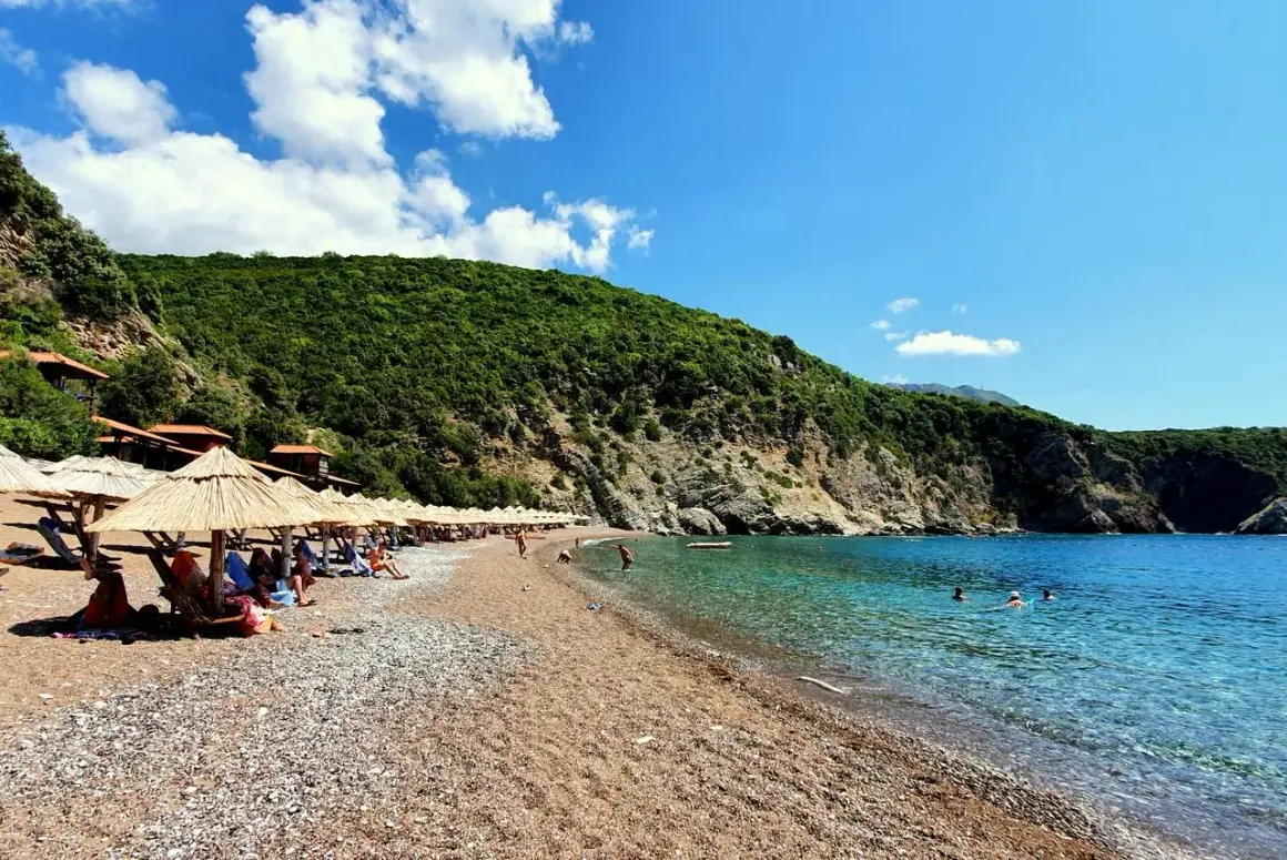 Słoneczne plaże w Budvie, z kamyczkami i piaskiem, otoczone zielonymi wzgórzami. Krystalicznie czysta woda Adriatyku zaprasza do kąpieli.