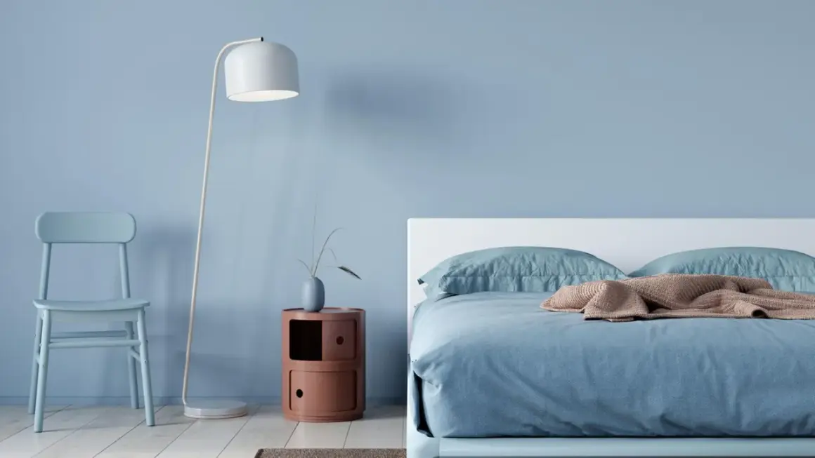 Ein hellblaues Schlafzimmer mit einem Bett, einem Stuhl und einem Nachttisch. Die schlafzimmer farbgestaltung wirkt beruhigend und modern.