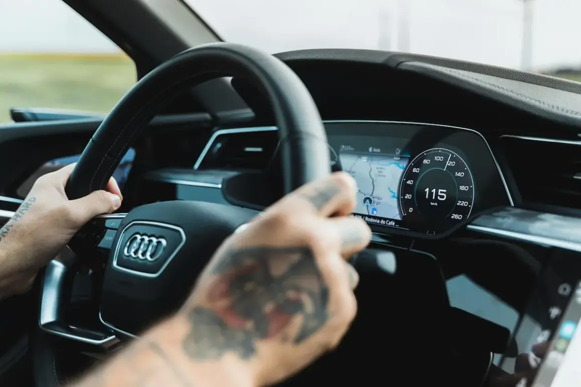 Ręce na kierownicy Audi A9, cyfrowy kokpit pokazuje 115 km/h.