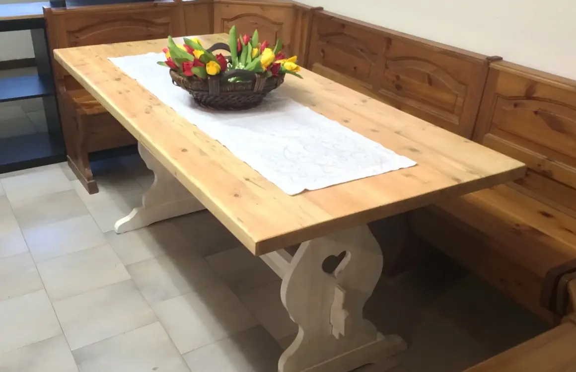 Tavolo in legno chiaro, pronto per essere lucidato, con un cestino di tulipani e una panca in legno scuro.