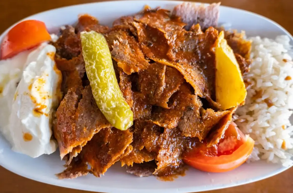 Pyszny kebab z mięsa mielonego, podany z ryżem, jogurtem, pomidorem i pikantną papryczką.