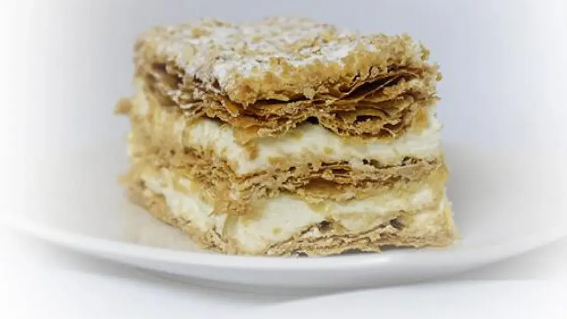 Deliciosa porción de costrada de Soria, con capas crujientes de hojaldre y crema suave, espolvoreada con azúcar glas.