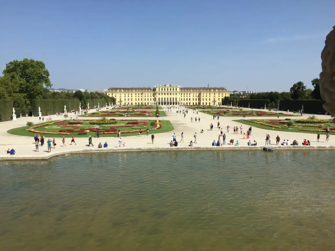 Piękny pałac Schönbrunn i jego ogrody, symbol wiedeńskiej historii. Ludzie spacerują pośród kwiatów i przy stawie.