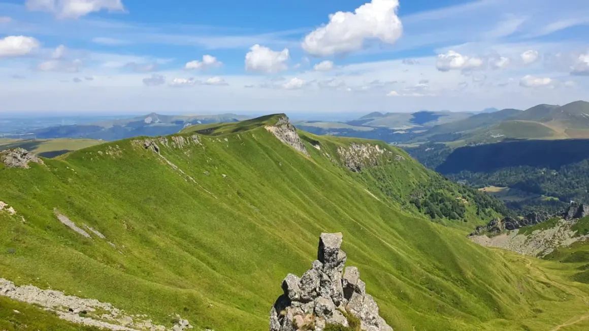 Zielone, faliste wzgórza Masywu Centralnego we Francji pod błękitnym niebem z chmurami.