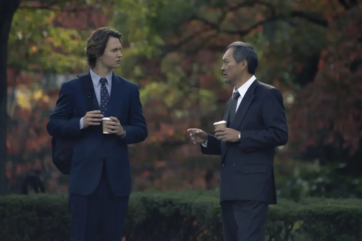 Zwei Männer in Anzügen, die Kaffee halten, diskutieren im Freien. Ein Mann ist jünger, der andere älter. Szene aus Tokyo Vice Staffel 2.