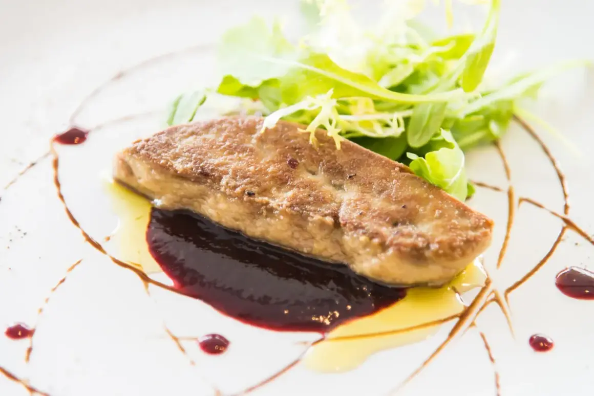 Tranche de foie gras poêlé, joliment assaisonné, servie avec une sauce aux fruits rouges et une salade verte croquante.