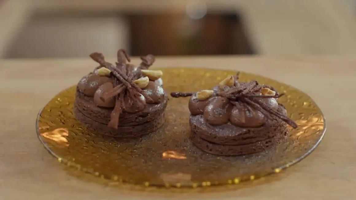 Dos bizcochos sin harina de chocolate, decorados con crema y avellanas, sobre un plato dorado.
