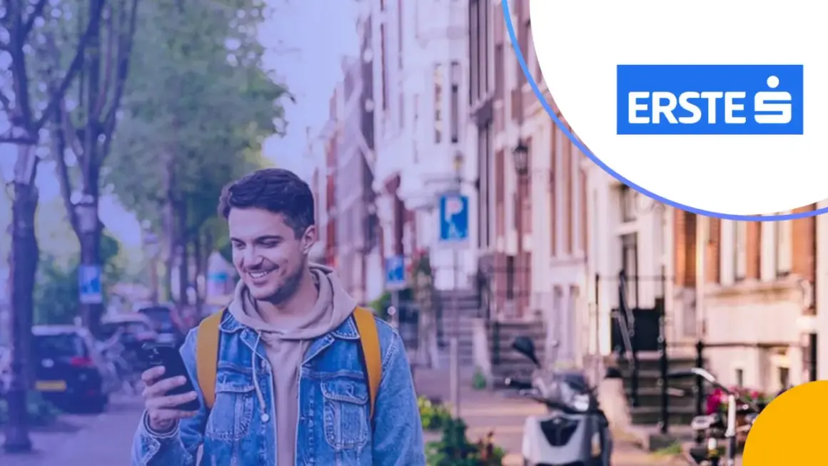 Uśmiechnięty mężczyzna z telefonem w ręku, w tle ulica z budynkami i skuterem. Promocja Santander lokata 3-miesięczna.