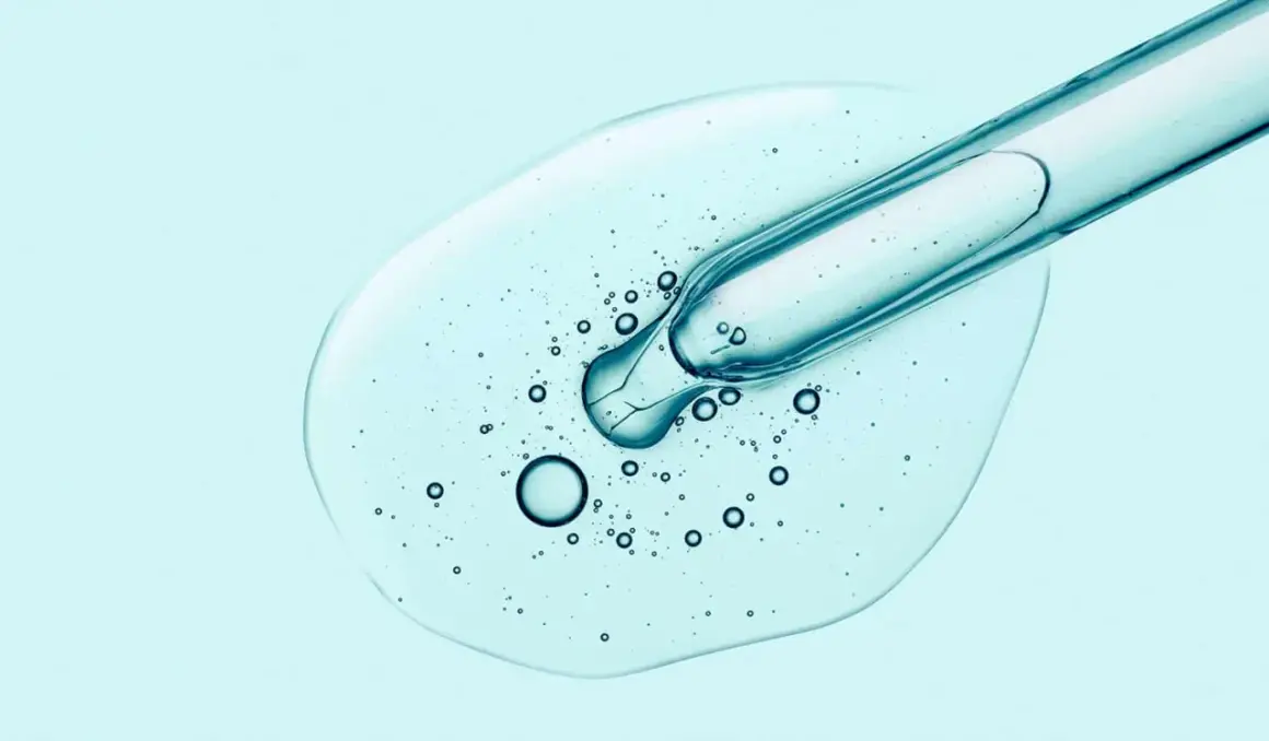 Tropfen Hyaluron-Serum aus Pipette auf hellblauem Hintergrund. Hilft gegen Pickel und spendet Feuchtigkeit.