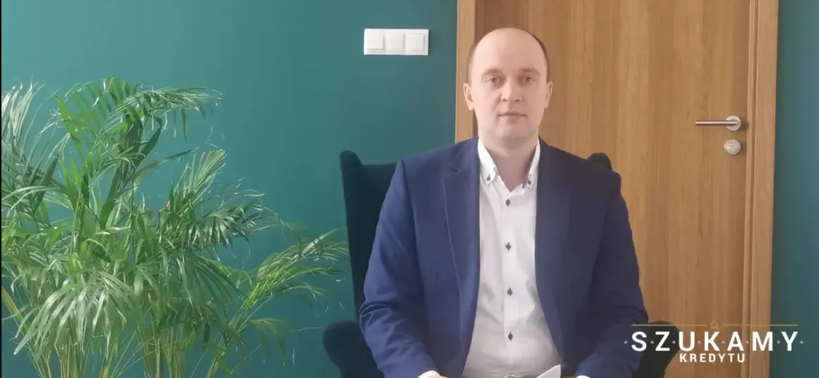 Mężczyzna w garniturze siedzi w fotelu obok rośliny.