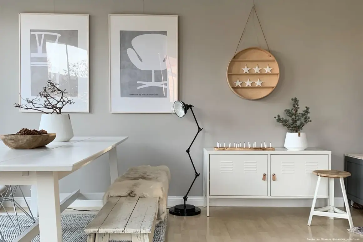 Ein Esszimmer im skandinavischen Stil mit einer warmen grau farbpalette. Ein weißer Tisch, eine Holzbank mit Schaffell und Kunstwerke an der Wand.