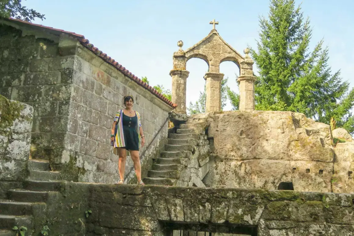 Mujer posa frente a la entrada del monasterio de San Pedro de Rocas, con su arquitectura de piedra y escalinata antigua.