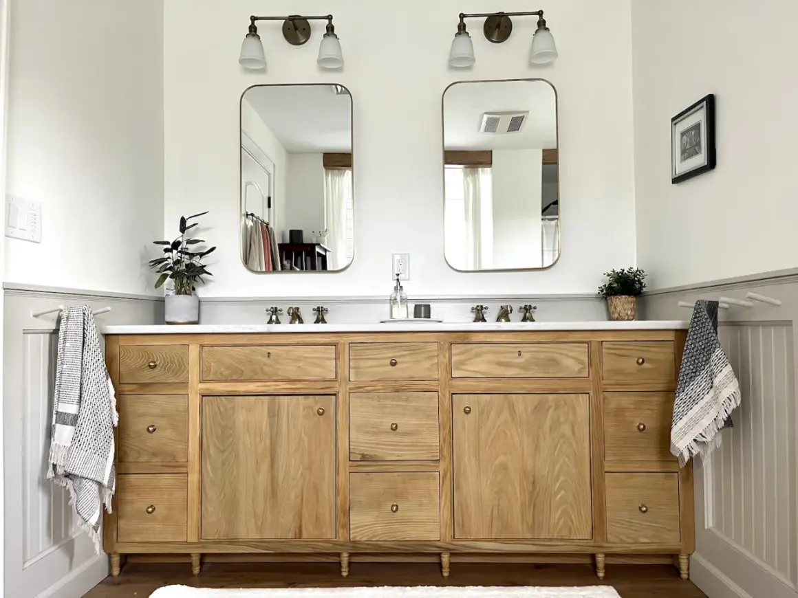 A beautiful DIY bathroom vanity with a natural wood finish, marble countertop, and brass fixtures. Two mirrors hang above, reflecting the bright, airy space.