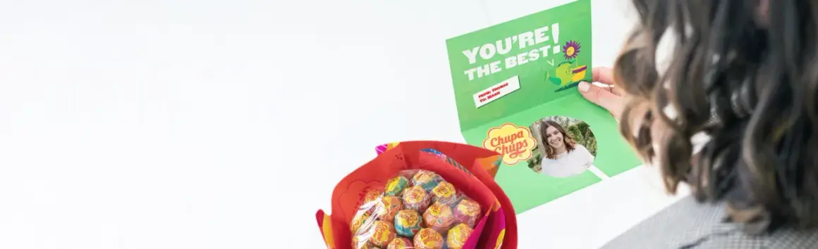 En person håller upp ett kort med texten "YOU'RE THE BEST" och en bild på sig själv. Bredvid syns en bukett med Chupa Chups-klubbor, en fin godis present diy.