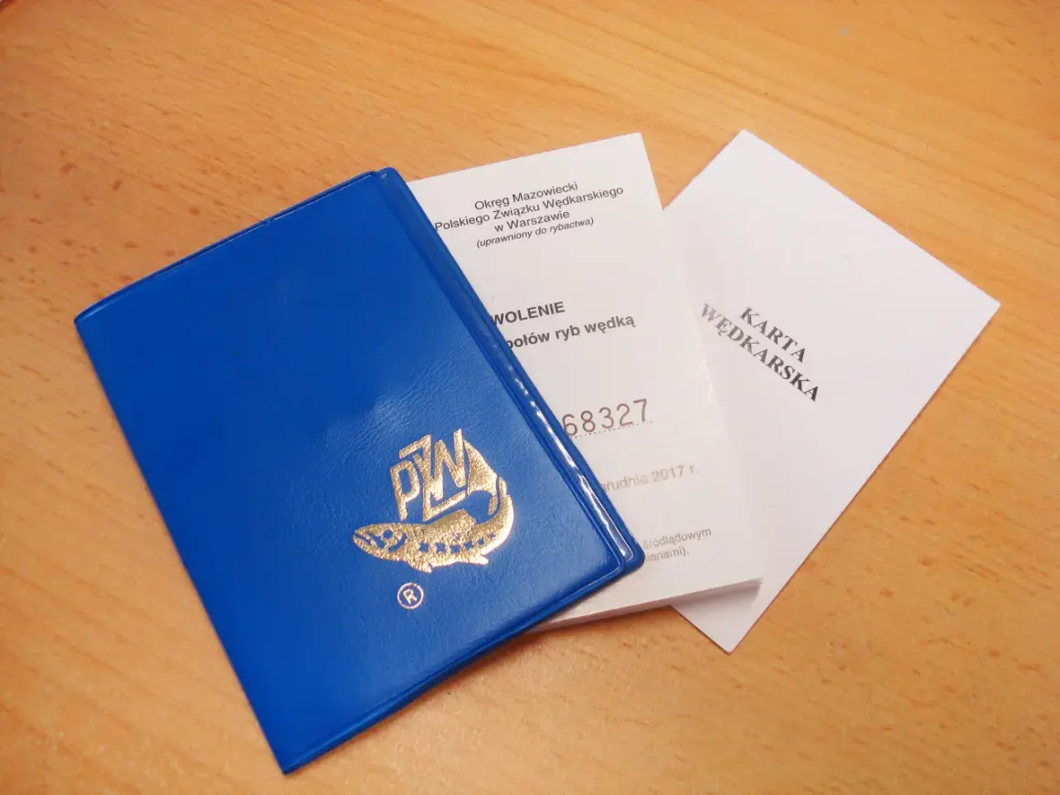 Niebieska książeczka z logo PZW i dokumenty "Karta Wędkarska" na drewnianym tle.