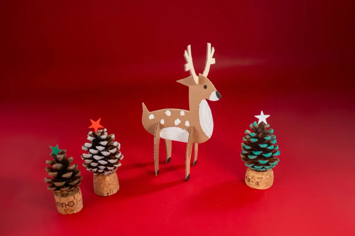 Julpynt med kottar: en papphjort och tre små julgranar gjorda av kottar, korkar och stjärnor.