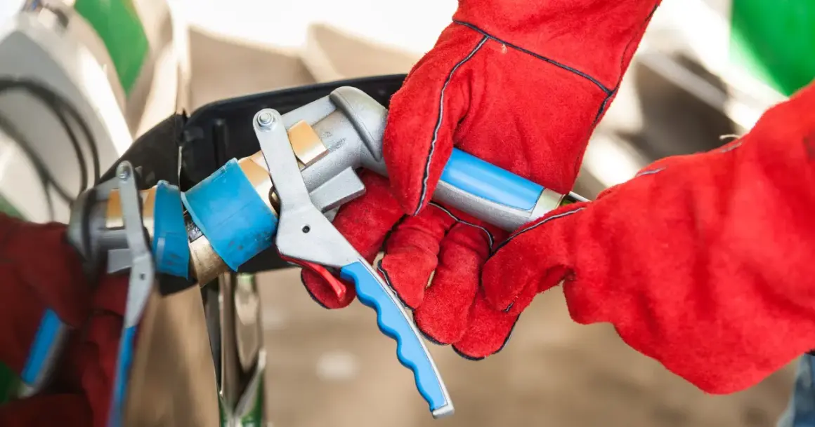 Ręce w czerwonych rękawicach podłączają pistolet do tankowania LPG. Sprawdzanie aktualnej lpg cena to klucz do oszczędności.