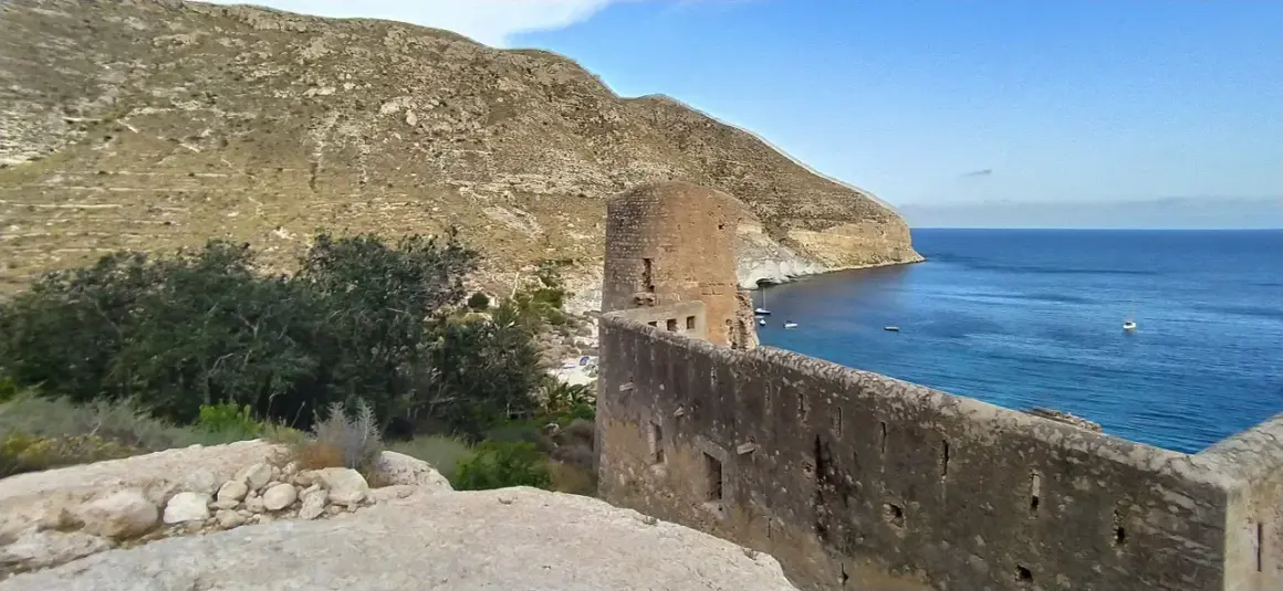 Ruinas de un castillo en cala san pedro, con el mar azul y montañas al fondo.